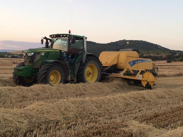 Tractor con empacadora de pacas grandes recogiendo paja al atardecer