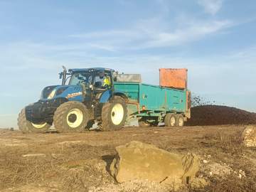 Tractor esparciendo estiércol junto a un sembrado