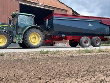 Tractor con remolque basculante nuevo delante de una nave
