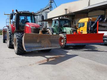 Dos tractores con pala frontal y un camión junto a unos silos