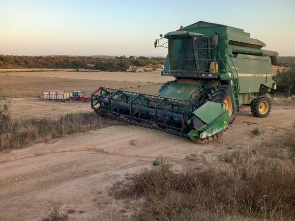 Cosechadora de cereal al atardecer con un tractor y un remolque de grano al fondo